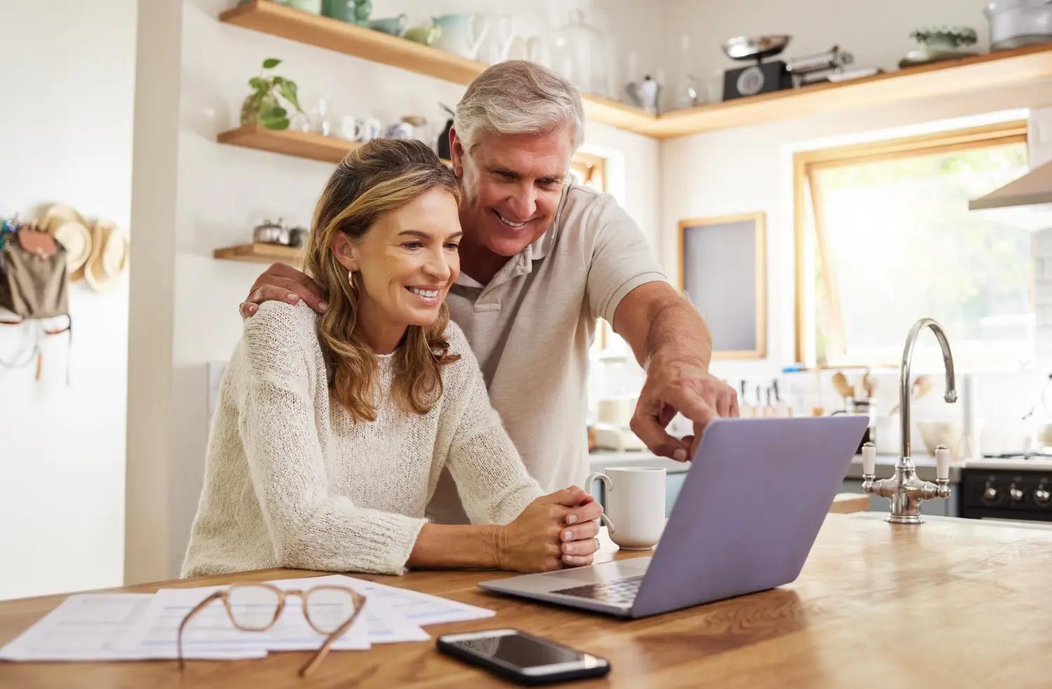 Glückliches Rentnerpaar mit Laptop und Unterlagen für die Ruhestandsplanung, eine Online-E-Commerce-Website oder eine digitale Bankanwendung für Investitionen.