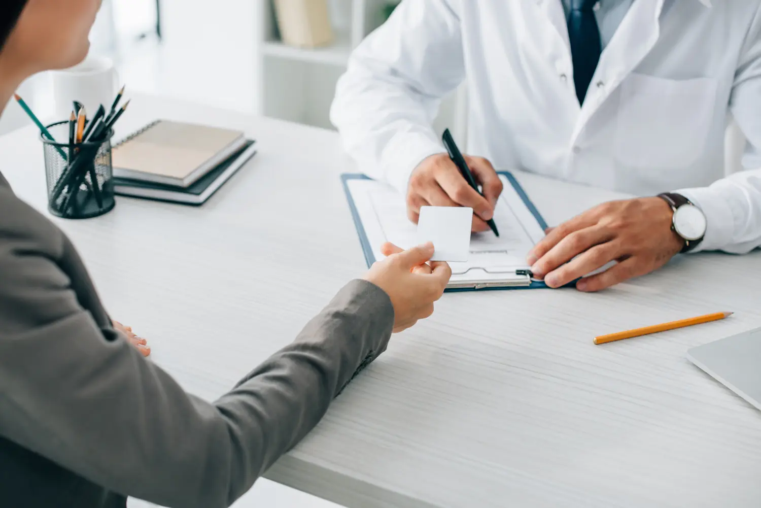 Beschnittenes Bild eines Patienten, der dem Arzt in der Klinik seinen Ausweis gibt, um das Versicherungsformular auszufüllen